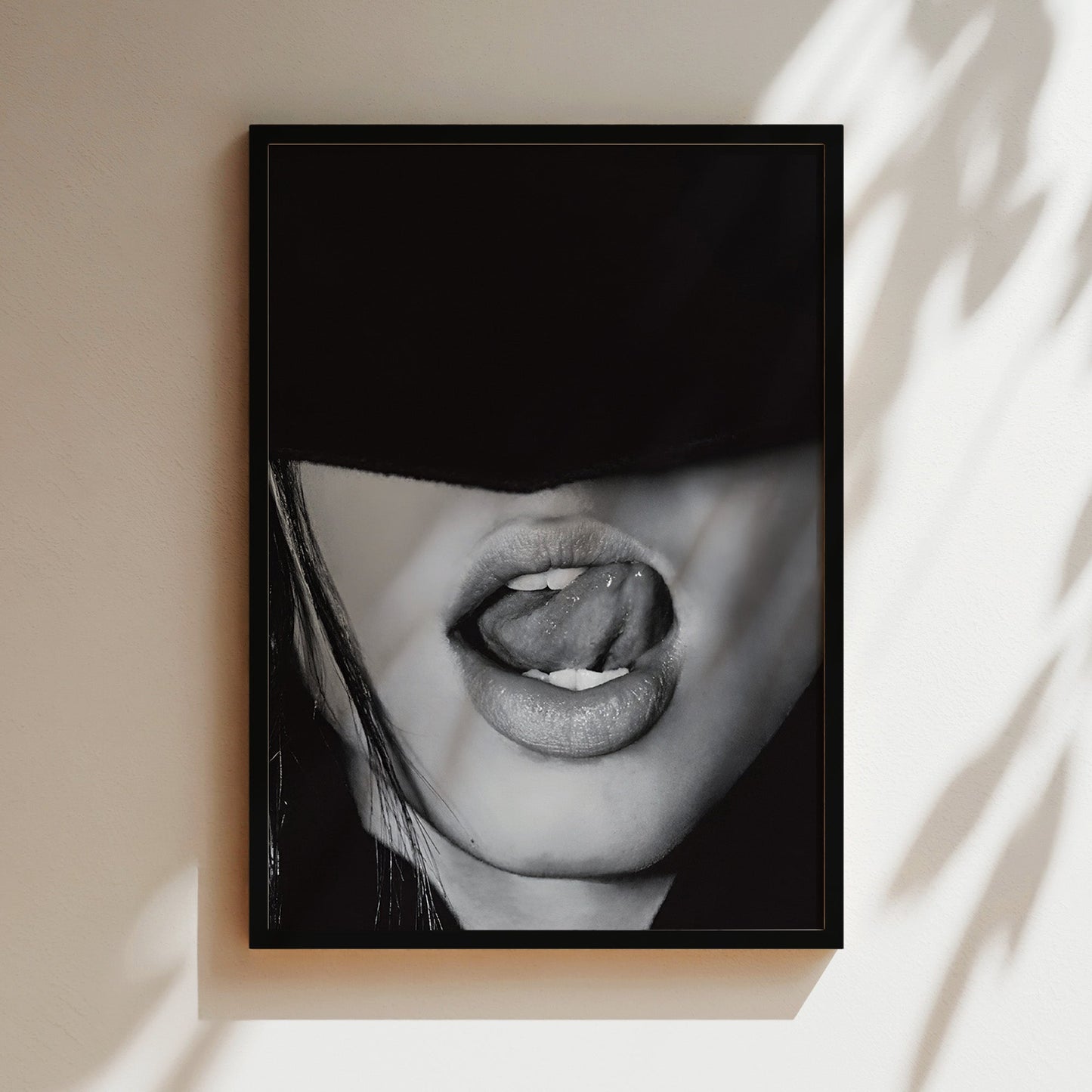 Black and white close-up of lips licking with seductive expression in a luxury black frame hanging on modern living room wall.