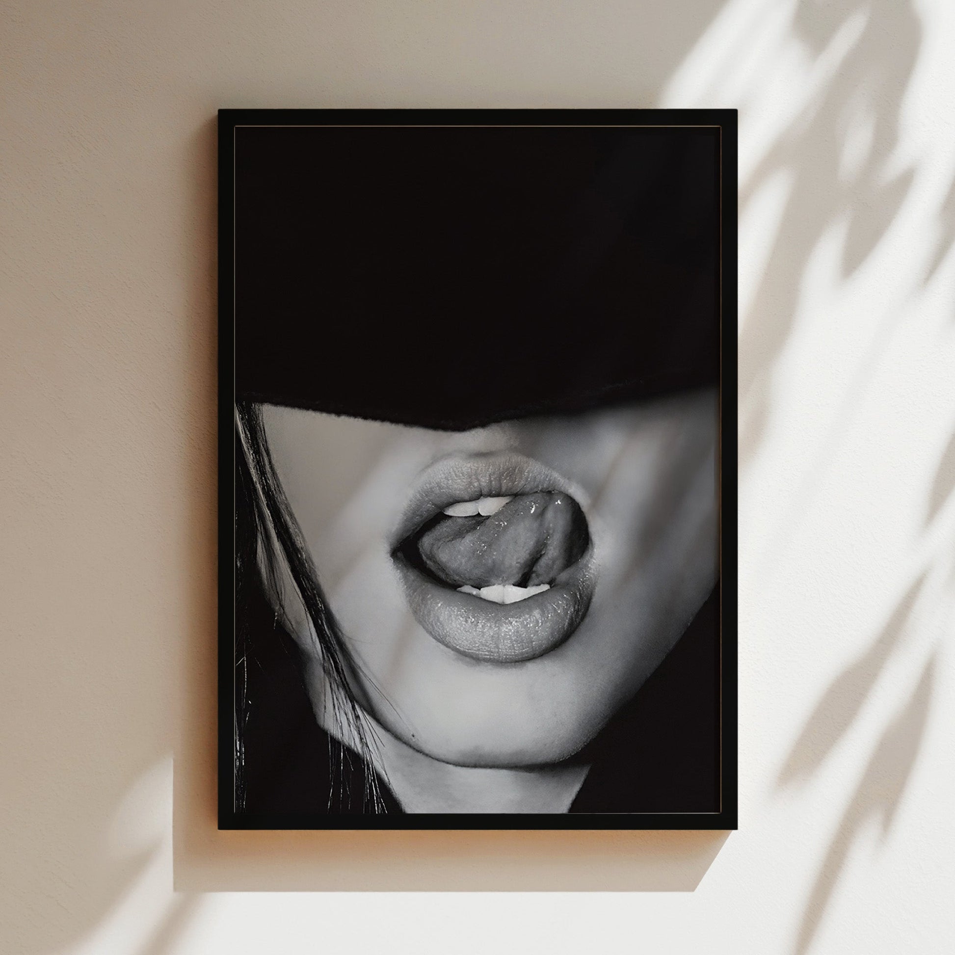 Black and white close-up of lips licking with seductive expression in a luxury black frame hanging on modern living room wall.